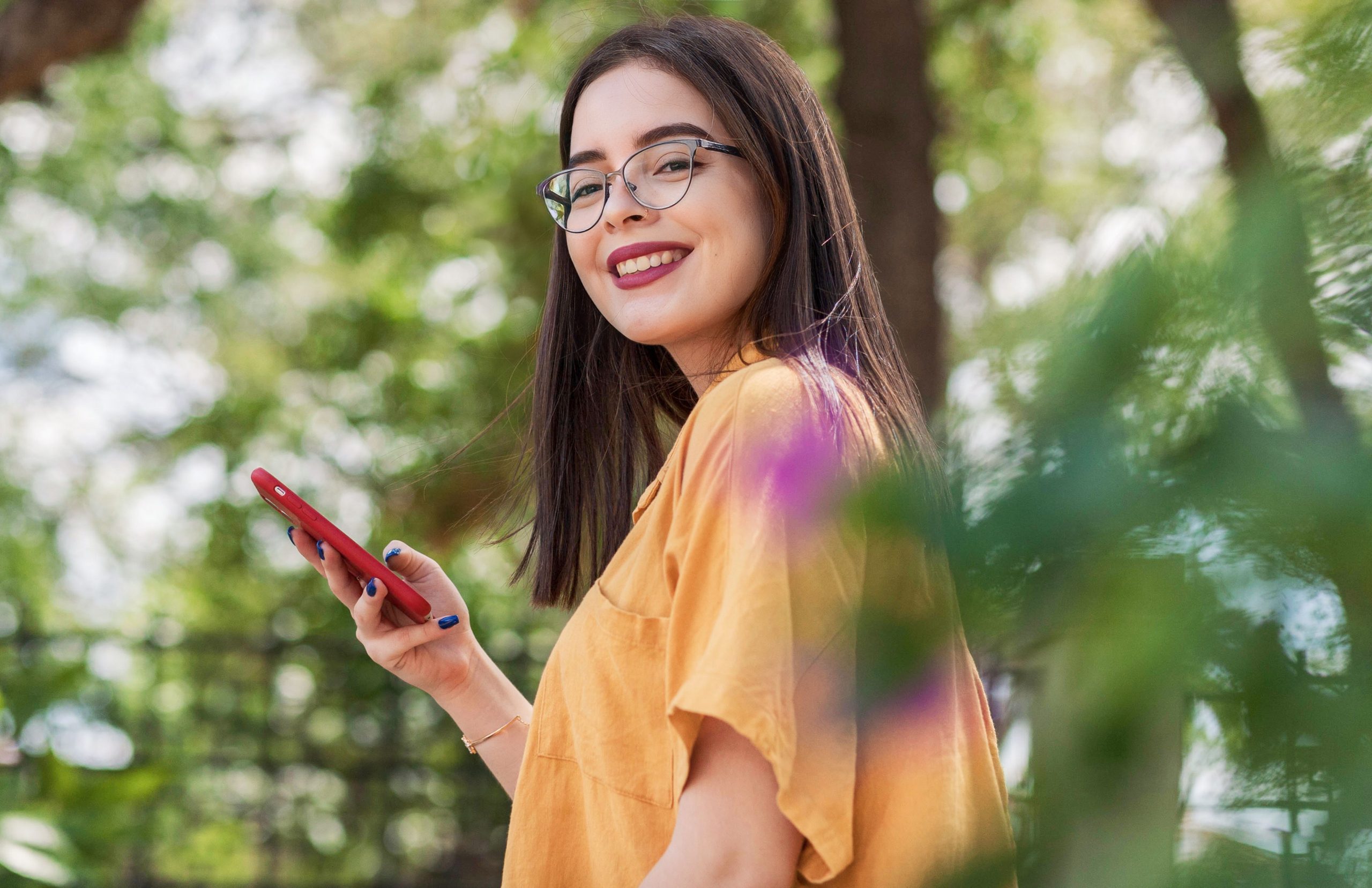 Una giovane donna sorridente in un ambiente luminoso mentre utilizza lo smartphone per chattare online.